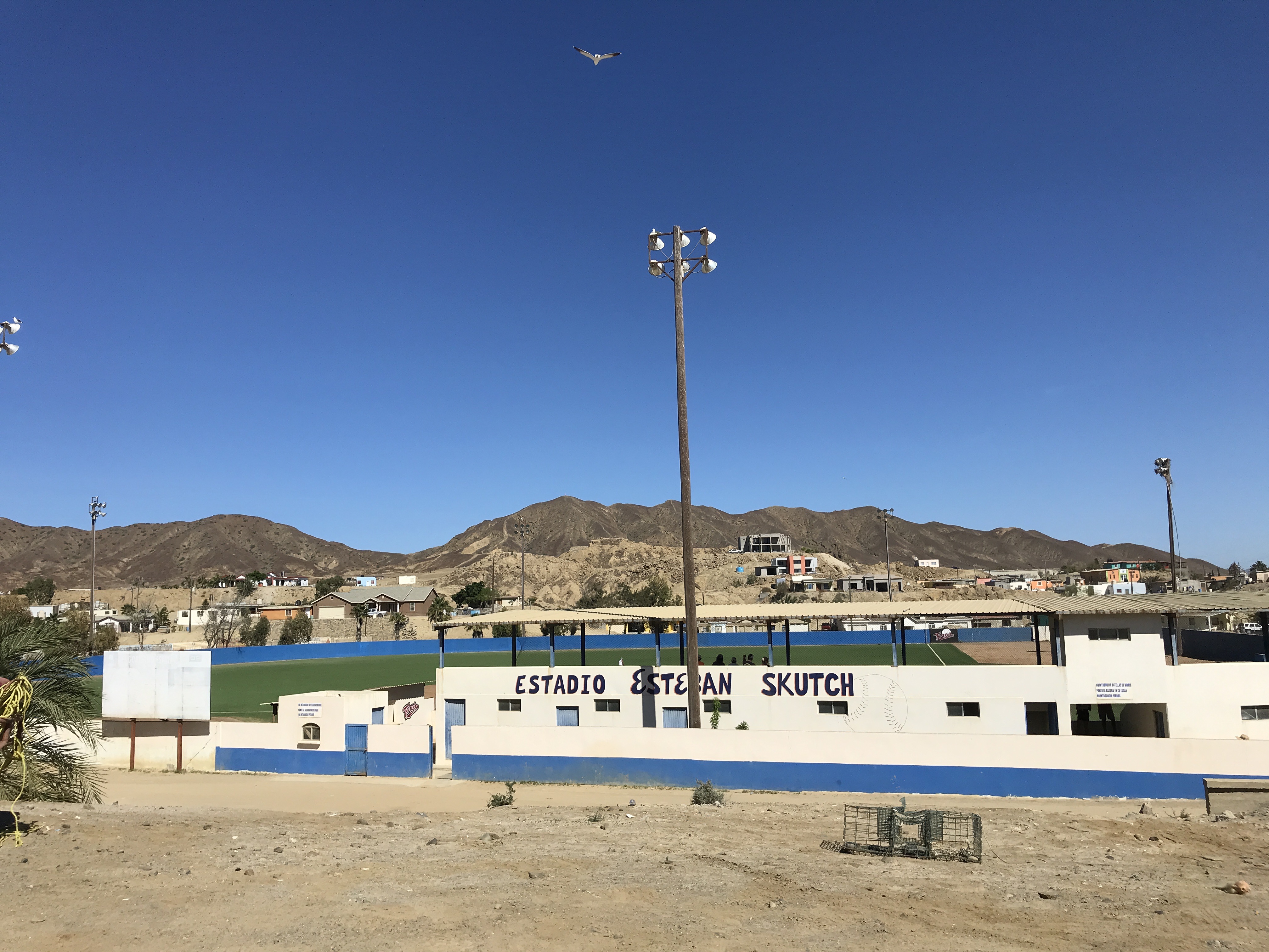 Baseball stadium with mountain in the background, the hand painted letters on the wall say "Estadio Esteban SKUTCH"