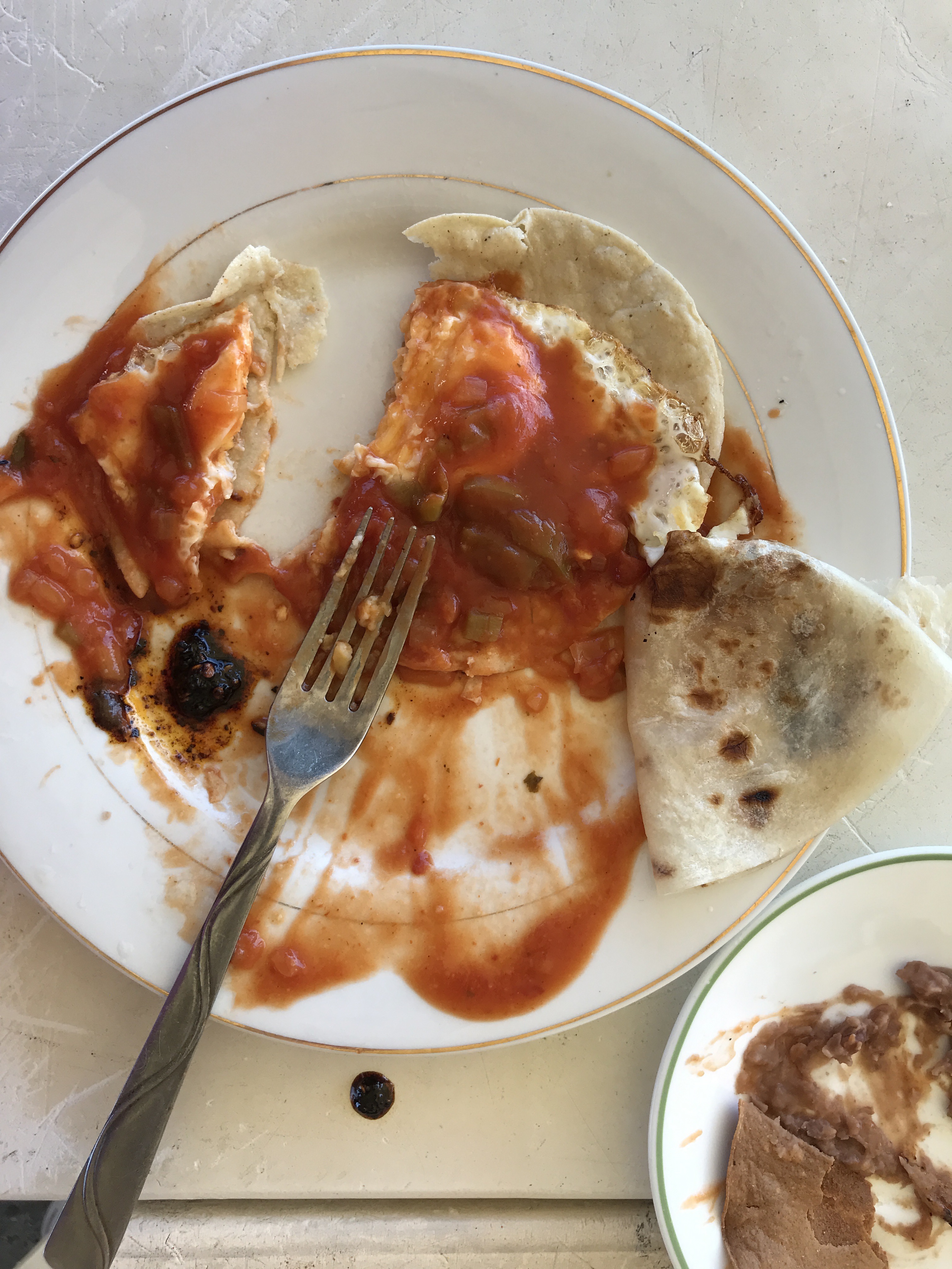 plate of half eaten huevos rancheros with folded flour tortilla and side of refried beans
