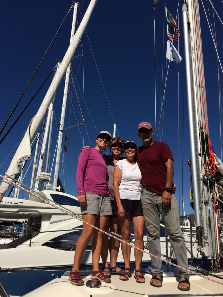 Four crew members are all smiles, arm in arm, on the SV Rapture foredeck, ready to cross the Pacific. 